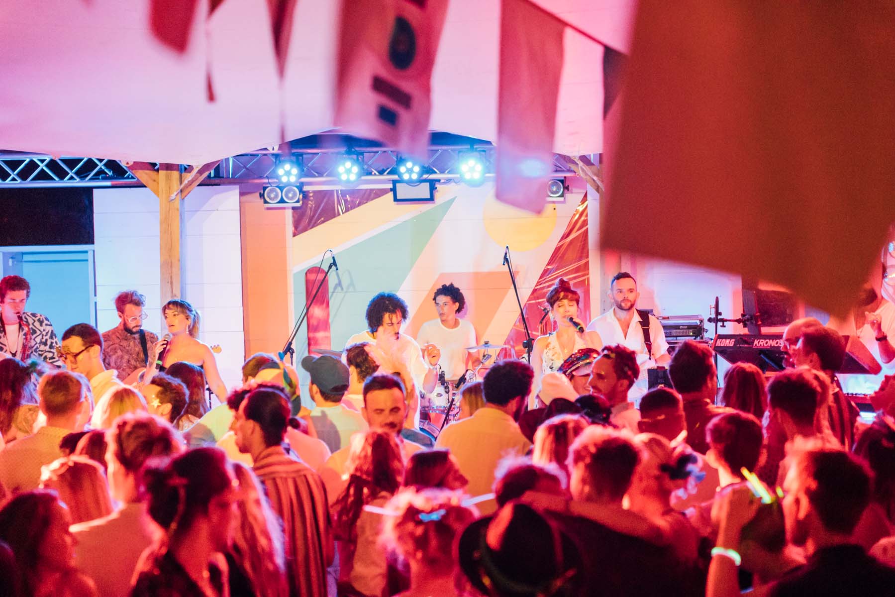 Crowd dancing to a band in a colourfully lit festival tent